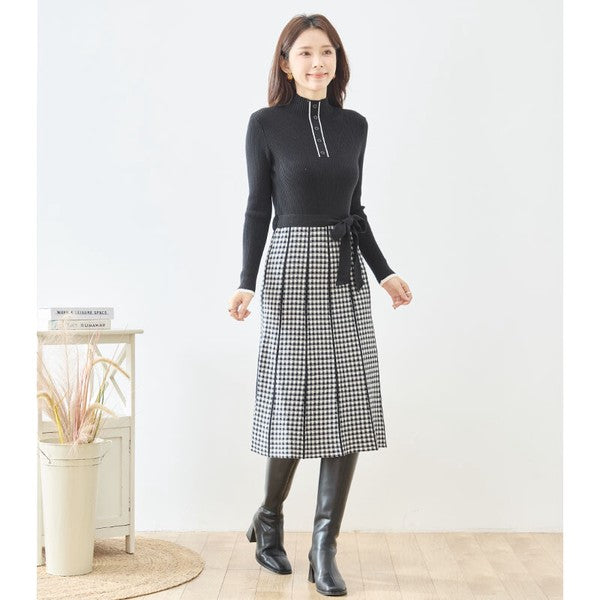 Mikonosublue Storeの黒いリブニットとチェック柄スカートを組み合わせたハイネックのドッキングワンピース。ウエストリボン付きでフィット&フレアのシルエット。