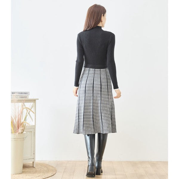 Mikonosublue Storeの黒いリブニットとチェック柄スカートがドッキングされたハイネックの長袖ワンピースを着用した女性の後ろ姿