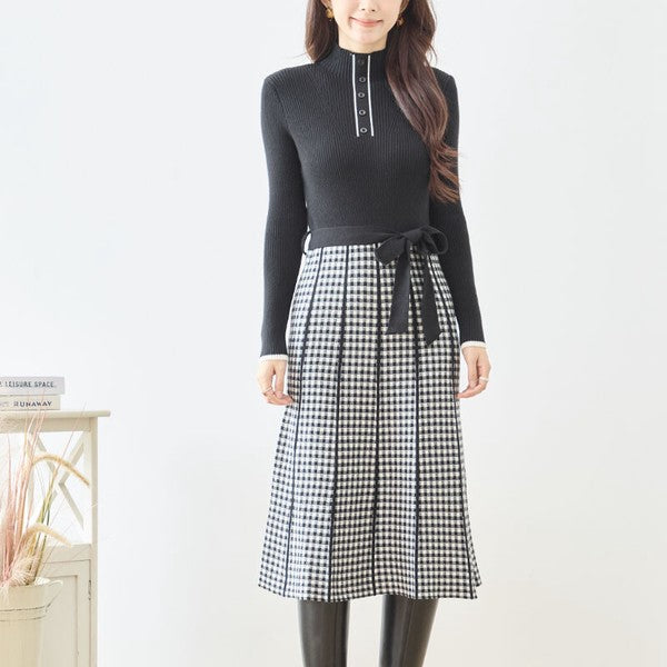 Mikonosublue Storeのハイネックニットワンピース。黒のリブニットとチェック柄フレアスカートのドッキングデザインで、ウエストリボン付きのフェミニンな秋冬スタイル。