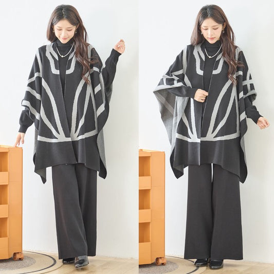 ブラックのポンチョ風ニットアウターを羽織ったモデルが正面を向いて立っている全身ショット。インナーはブラックで統一された大人のモードスタイル。ブラック