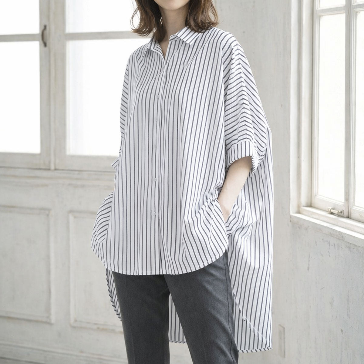 ホワイト×ブラックのストライプ柄ドルマンスリーブチュニックシャツを着用したモデル。春夏に相応しい清涼感のある大人カジュアルスタイル。
