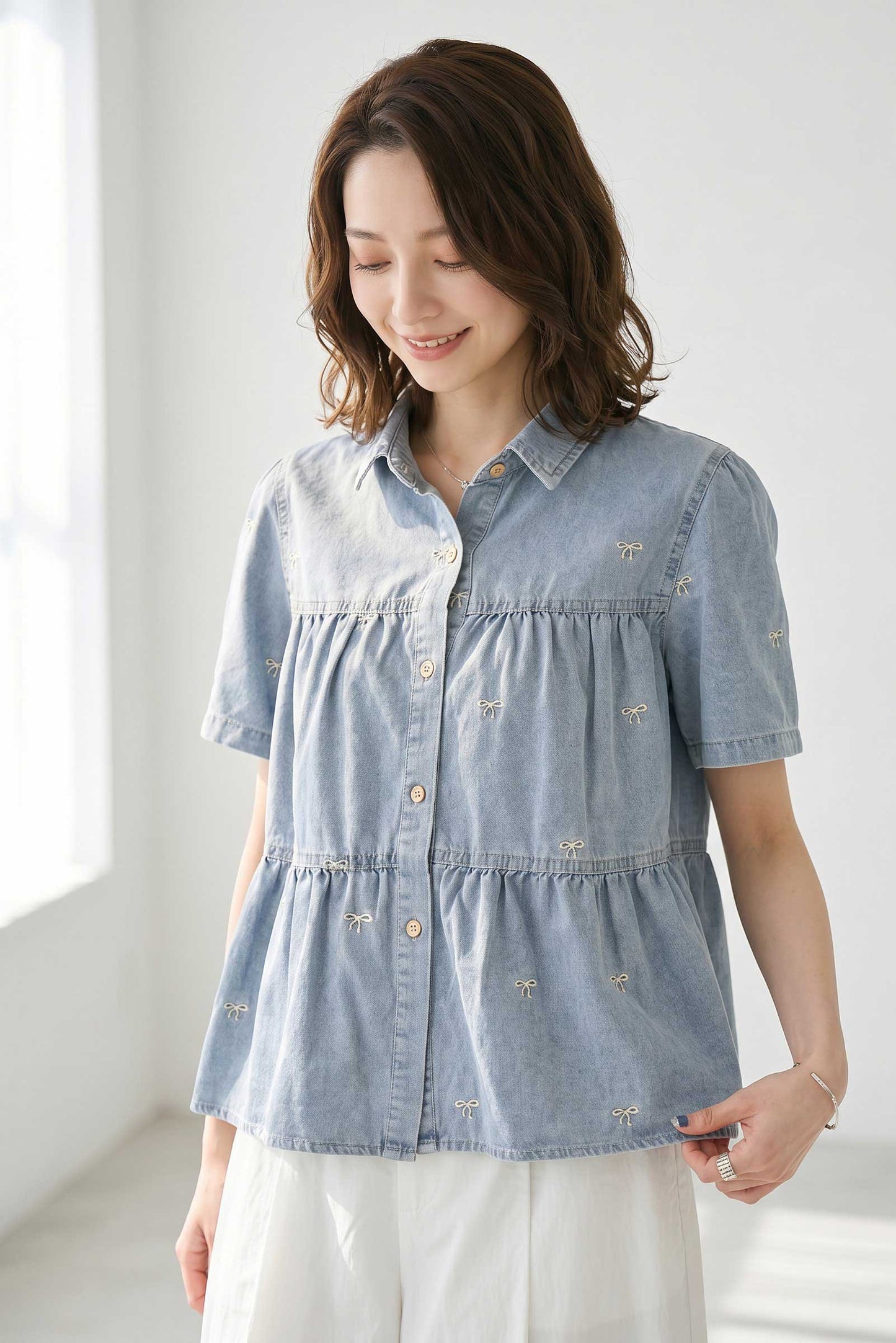 小さなリボン柄の刺繍が全体にあしらわれた、ダンガリー素材の半袖ティアードシャツブラウス。胸元の切り替えギャザーが大人可愛い春夏のトップス。