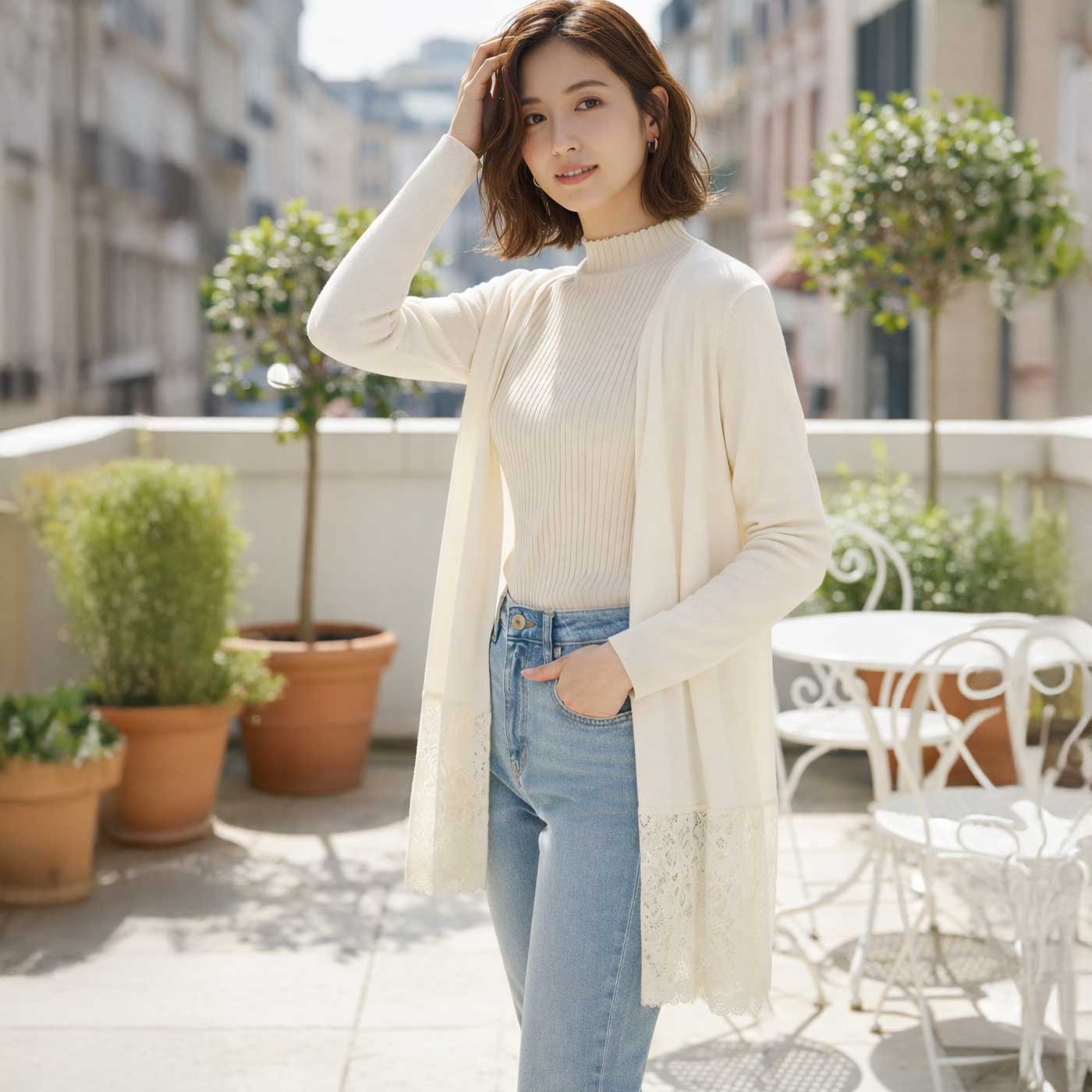 裾に繊細なレースをあしらったアイボリーのトッパーカーディガンを着用したモデル。春夏にぴったりの軽やかで上品な羽織りスタイル。