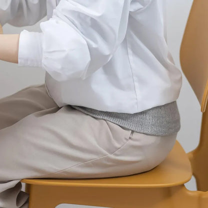 女性が椅子に座ってグレーの腹巻を装着している様子（横向き）