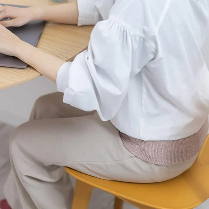 腰を温めるために腹巻を巻いて座っている女性