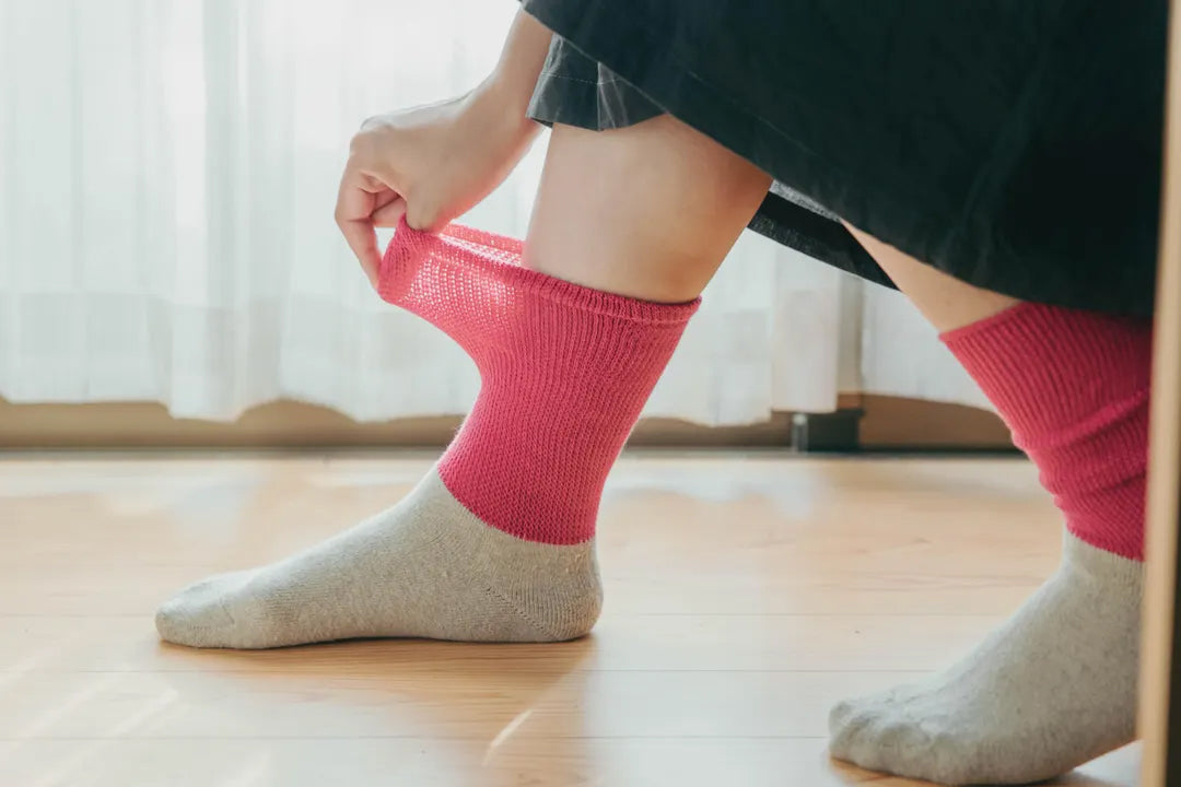 ピンクのソックスを足に通す様子（ナチュラルな室内光）