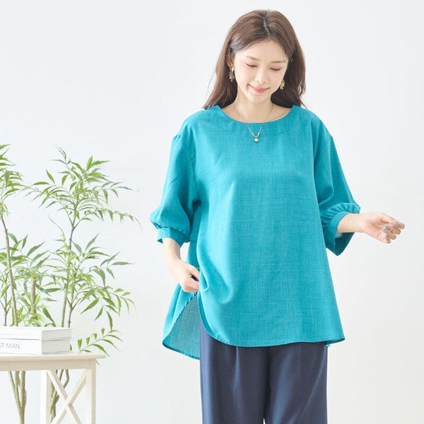 Mikonosublue Storeのバックフリルが特徴的なターコイズブルーの5分袖Aライントップスを着用した女性