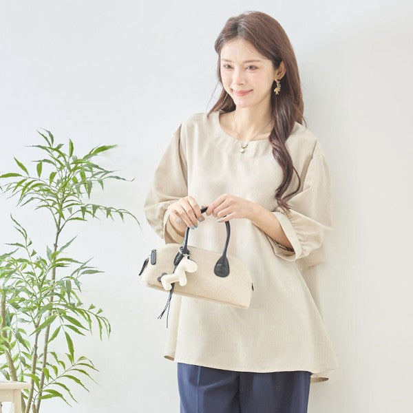 Mikonosublue Storeのベージュのバックフリルトップス。ゆったりとしたAラインの5分袖で、二の腕をカバーする上品な夏用ブラウスを着用した女性。
