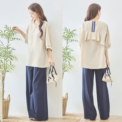 Mikonosublue StoreのベージュのバックフリルAライントップス。5分袖でゆったりとしたシルエット、後ろ姿にファスナーとフリルが施された夏用ブラウス。
