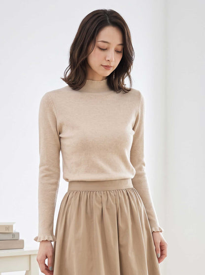 Mikonosublue Storeのベージュのハイネックリブニットプルオーバー。首元と袖口にさりげないフリルがあしらわれた、上品でフェミニンな長袖トップス。