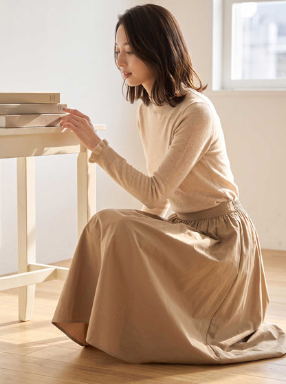 Mikonosublue Storeのベージュのリブニットプルオーバー。首元と袖口にフリルがあしらわれたハイネックデザインで、柔らかな素材感が特徴。