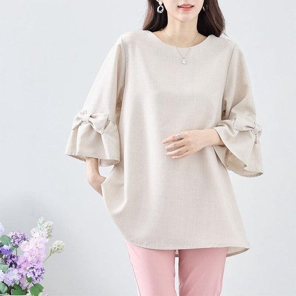 Mikonosublue Storeのベージュの七分袖チュニック。袖のリボンとふんわりとしたAラインシルエットが特徴で、体型カバーも叶う上品なポリエステル素材のブラウス。