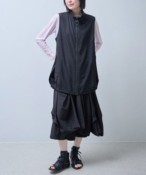 Mikonosublue Storeの黒いロングジレ。大きなリングジップと丸ポケットが特徴で、裾がゴム仕様のコクーンシルエット。軽量なポリスパン素材で、Tシャツと重ね着したモードな着こなし。