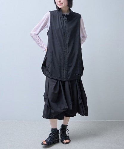 Mikonosublue Storeの黒いロングジレ。大きなリングジップと丸ポケットが特徴で、裾がゴム仕様のコクーンシルエット。軽量なポリスパン素材で、Tシャツと重ね着したモードな着こなし。