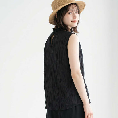 Mikonosublue Storeの黒い綿ローン素材のクリンクル加工ノースリーブブラウス。首元のフリルとバックボタンが特徴的で、麦わら帽子を被った女性が着用している後ろ姿。