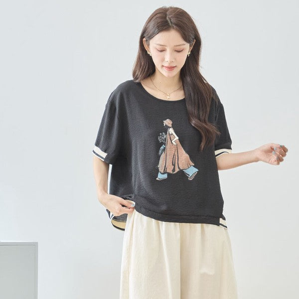 Mikonosublue Storeのファッションイラストがプリントされた黒のゆったり半袖トップス。配色リブがアクセント。