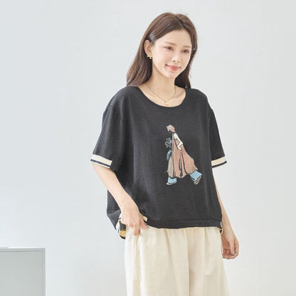 Mikonosublue Storeのファッションイラストがプリントされた黒のゆったり半袖トップス。配色リブがアクセントの大人カジュアルなデザイン。