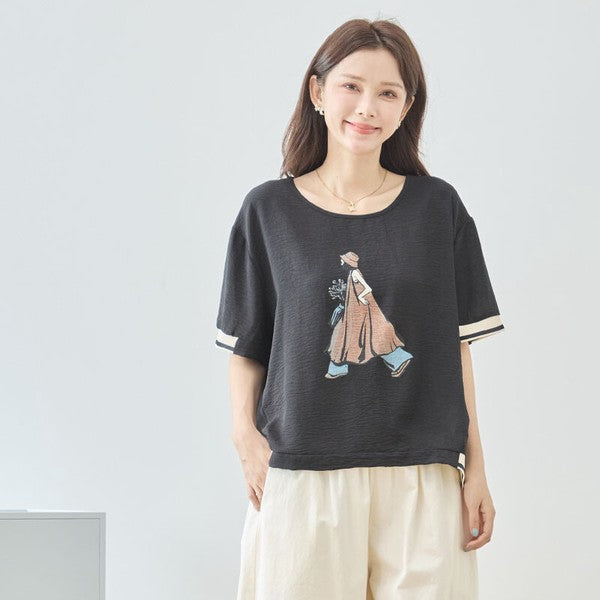 Mikonosublue Storeの黒い半袖トップス。女の子のイラストプリントと袖口の配色リブが特徴のゆったりとしたシボ感素材。