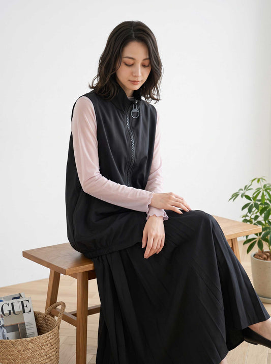 Mikonosublue Storeの黒いロングジップベストを着用し、ベンチに座る女性。リングジップと丸ポケットが特徴の軽量なレイヤードスタイル。
