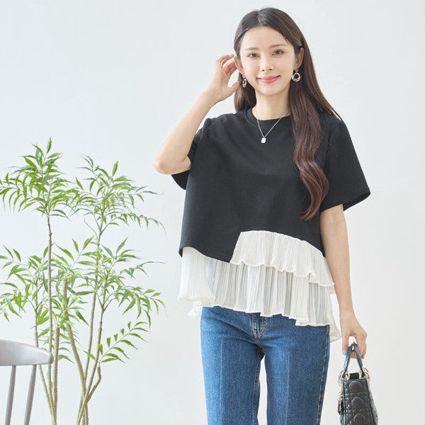 Mikonosublue Storeの黒い半袖Tシャツ。裾に白いアシンメトリーな2段ティアードプリーツフリルをあしらった異素材切り替えデザインで、体型カバーも叶うエレガントなトップス。