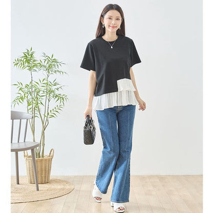 Mikonosublue Storeの黒い半袖Tシャツ。裾に白いアシンメトリーなプリーツフリルをあしらった異素材切り替えデザインで、デニムパンツと合わせたフェミニンなスタイル。