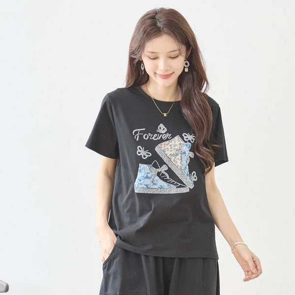 Mikonosublue Storeのラインストーンと異素材パッチワークのスニーカー柄が施された黒の半袖Tシャツを着た女性