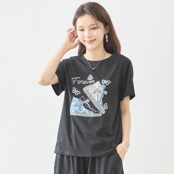 Mikonosublue Storeのラインストーンと異素材パッチワークのスニーカー柄が施された黒の半袖Tシャツを着た女性