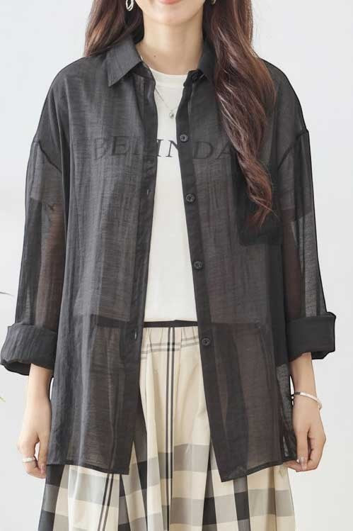 Mikonosublue Store black sheer long-sleeve shirt with lace details and a relaxed fit, worn over a white t-shirt.