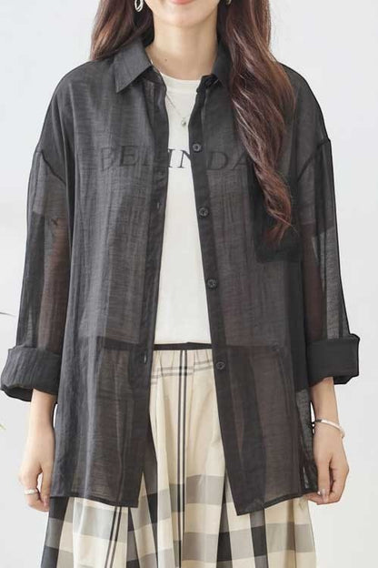 Mikonosublue Store black sheer long-sleeve shirt with lace details and a relaxed fit, worn over a white t-shirt.