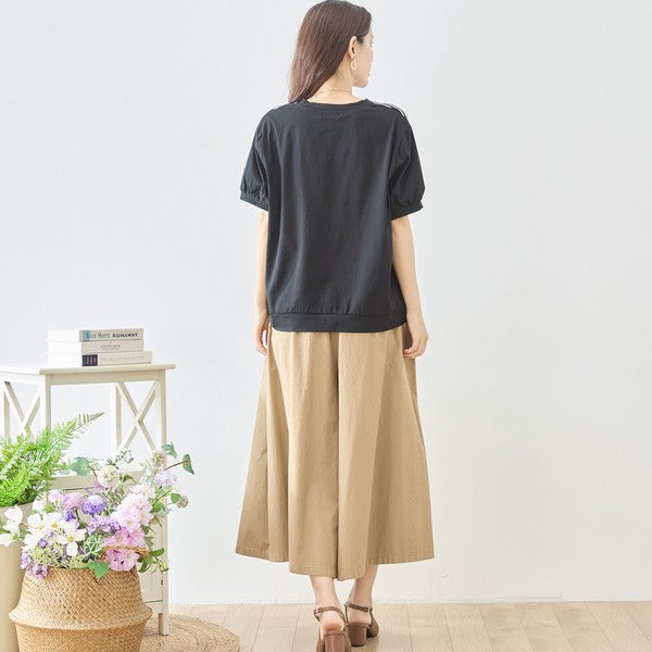 Mikonosublue Storeの黒い無地半袖Tシャツを着用し、ベージュのワイドパンツを合わせた後ろ姿の女性