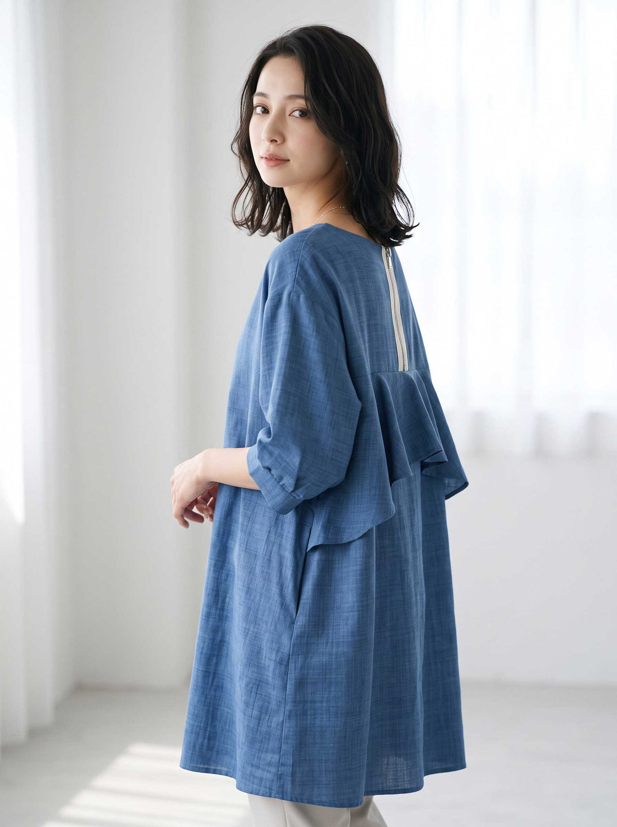 Mikonosublue Storeのバックフリルが特徴的なブルーの5分袖Aライントップスを着用した女性のバックスタイル