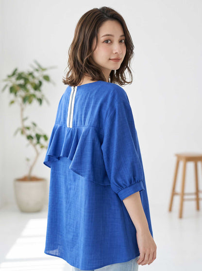 Mikonosublue Storeのバックフリルが特徴的な青い5分袖Aライントップスを着用した女性のバックスタイル