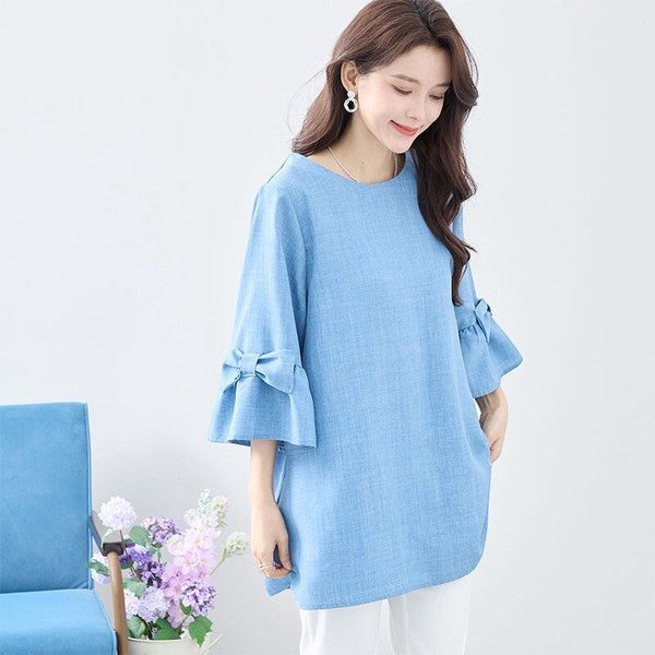 Mikonosublue Storeの袖にリボンがあしらわれた水色の七分袖Aラインチュニックブラウス。ゆったりとしたシルエットで体型カバーも叶うフェミニンなトップス。
