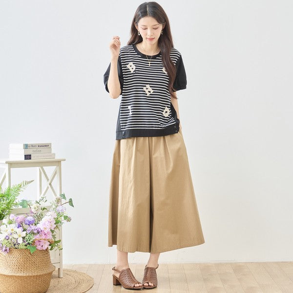 Mikonosublue Storeのアルファベット刺繍入りボーダー切り替えTシャツを着用した女性。黒の半袖トップスにベージュのワイドパンツを合わせた大人カジュアルなコーディネート。