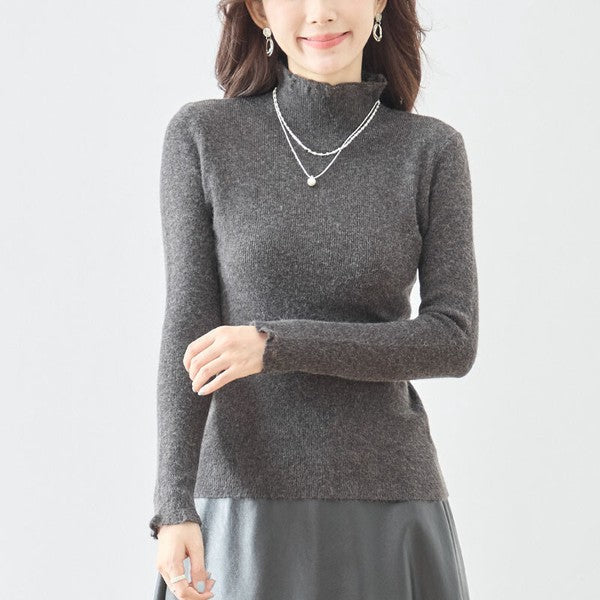 Mikonosublue Storeのチャコールグレーのハイネックリブニットプルオーバー。首元と袖口にフェミニンなフリルがあしらわれた、伸縮性のある長袖インナー。