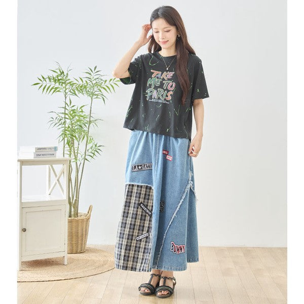 Mikonosublue Storeのデニムとチェック柄を切り替えたパッチワークマキシスカート。ワッペンとフリンジが特徴のリメイク風デザインで、ウエストゴム仕様のコットン製ロングスカートを着用した女性。