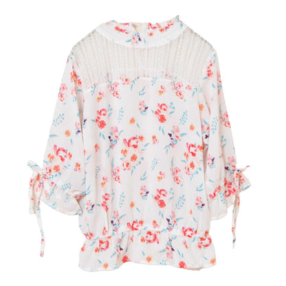 Mikonosublue Storeのデコルテに繊細なレースをあしらった、ホワイトベースの花柄ジョーゼットブラウス。袖口のリボンとペプラム風の裾がフェミニンな七分袖トップス。