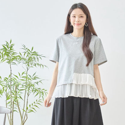Mikonosublue Storeのグレーの半袖Tシャツ。裾にアシンメトリーな白いプリーツフリルをあしらった異素材切り替えデザインで、体型カバーも叶えるフェミニンなトップス。