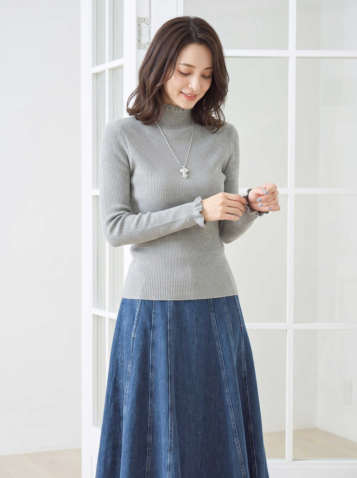 Mikonosublue Storeのグレーのリブニットプルオーバー。首元と袖口のフリルが特徴のハイネック長袖トップス。