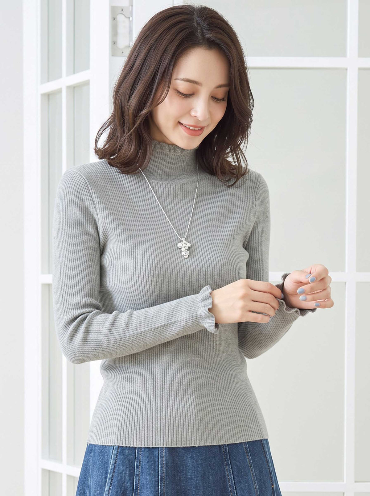 Mikonosublue Storeのグレーのリブニットプルオーバー。首元と袖口にフリルがあしらわれたハイネックの長袖トップス。
