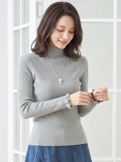 Mikonosublue Storeのグレーのリブニットプルオーバー。首元と袖口にフリルがあしらわれたハイネックの長袖トップス。