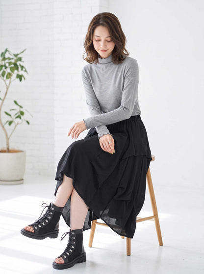 Mikonosublue Storeのグレーのハイネックリブカットソー。首元と袖口にメロウフリルをあしらった長袖インナーで、黒のスカートと合わせた大人可愛いレイヤードスタイル。