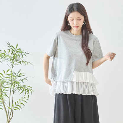 Mikonosublue Storeのグレーの半袖Tシャツ。裾に白いアシンメトリーなプリーツフリルをあしらった異素材切り替えデザインで、体型カバーも叶えるフェミニンなトップス。