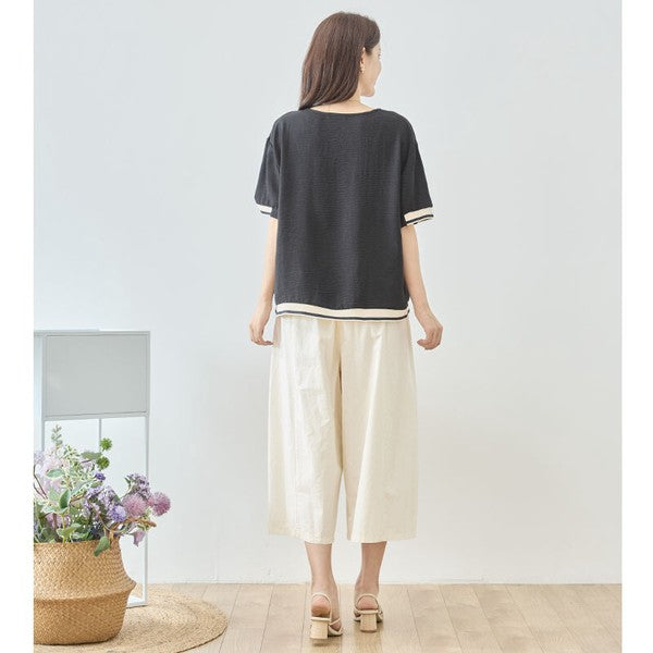 Mikonosublue Storeの配色リブがアクセントになった黒の半袖トップスを着用し、白のワイドパンツと合わせた後ろ姿