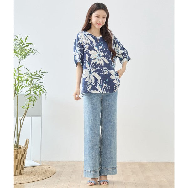 Mikonosublue Storeのネイビー地に白い大きな花柄がプリントされた綿100%のドルマン袖トップスを着用した女性