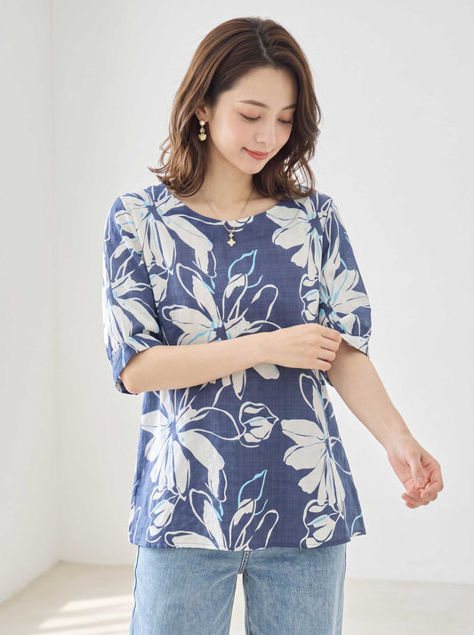 Mikonosublue Storeのネイビー地に白い大きな花柄がプリントされた綿100%のゆったりとしたドルマン袖トップスを着た女性