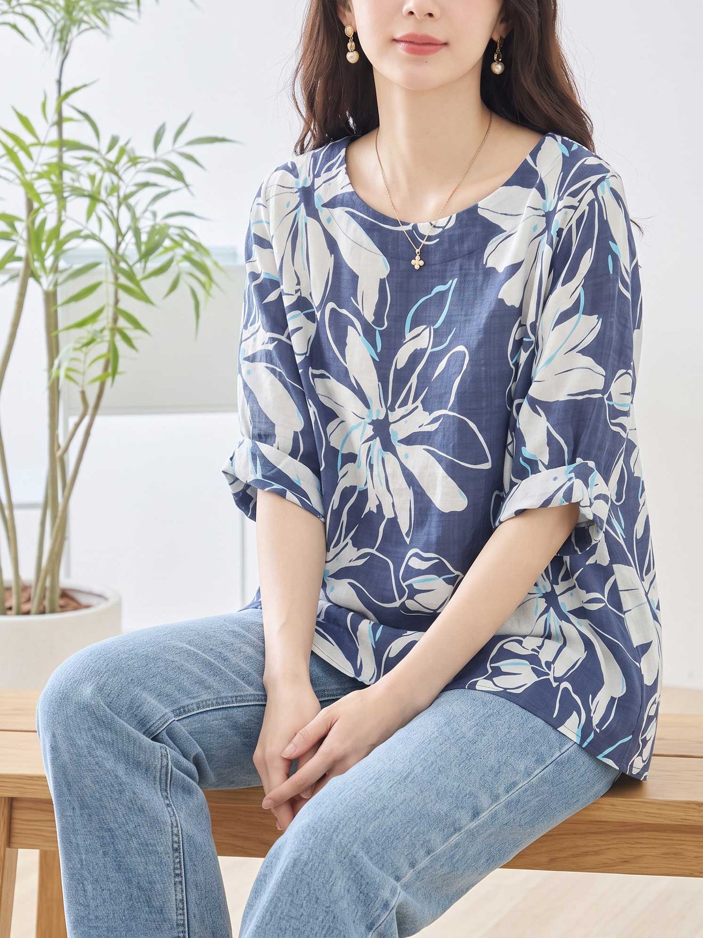 Mikonosublue Storeのネイビー地に白い大きな花柄がプリントされた綿100%のゆったりとしたドルマンスリーブトップスを着用した女性