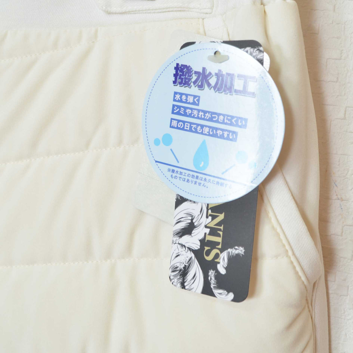 Mikonosublue Storeの撥水加工が施されたアイボリーのキルティングダウンパンツ。タグ付きのクローズアップ。