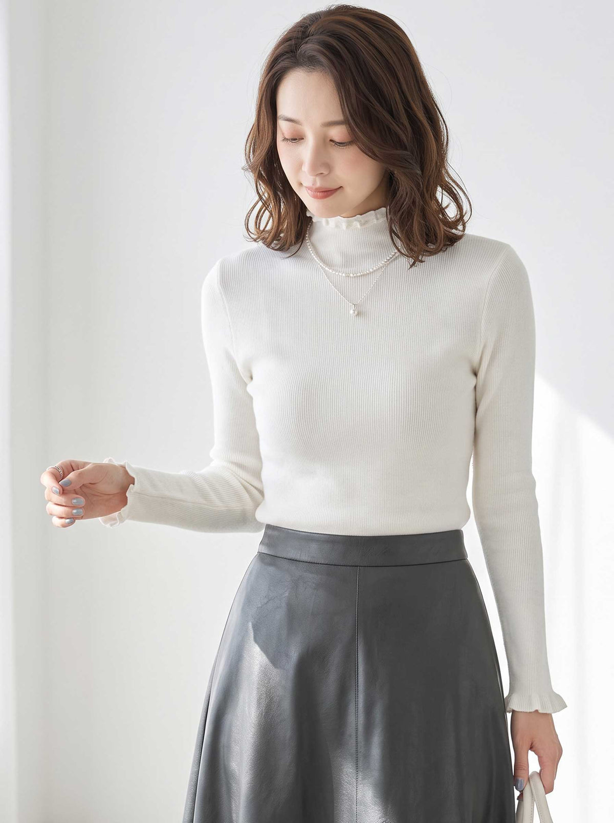 Mikonosublue Storeのアイボリー色のリブニットプルオーバー。首元と袖口にフリルがあしらわれたハイネックデザインで、上品なシルエットが特徴。