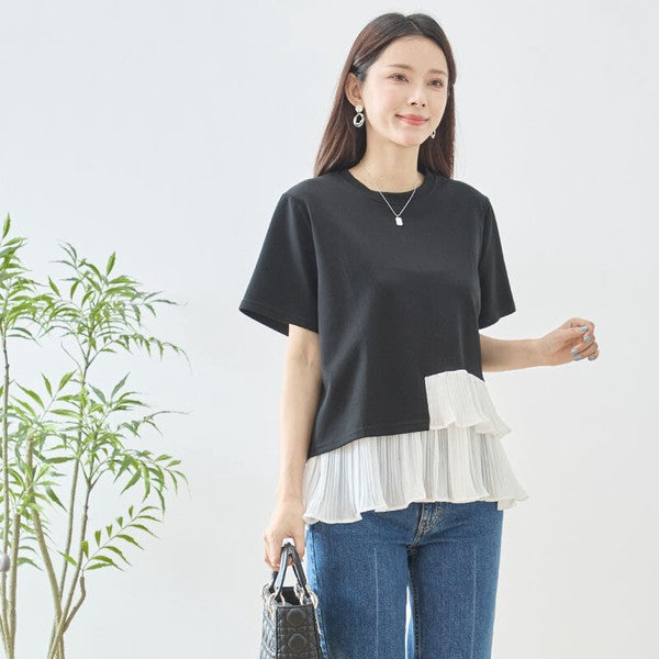 Mikonosublue Storeの黒い半袖Tシャツ。裾に白いアシンメトリーなプリーツフリルをあしらった異素材切り替えデザインで、体型カバーも叶えるフェミニンなトップス。